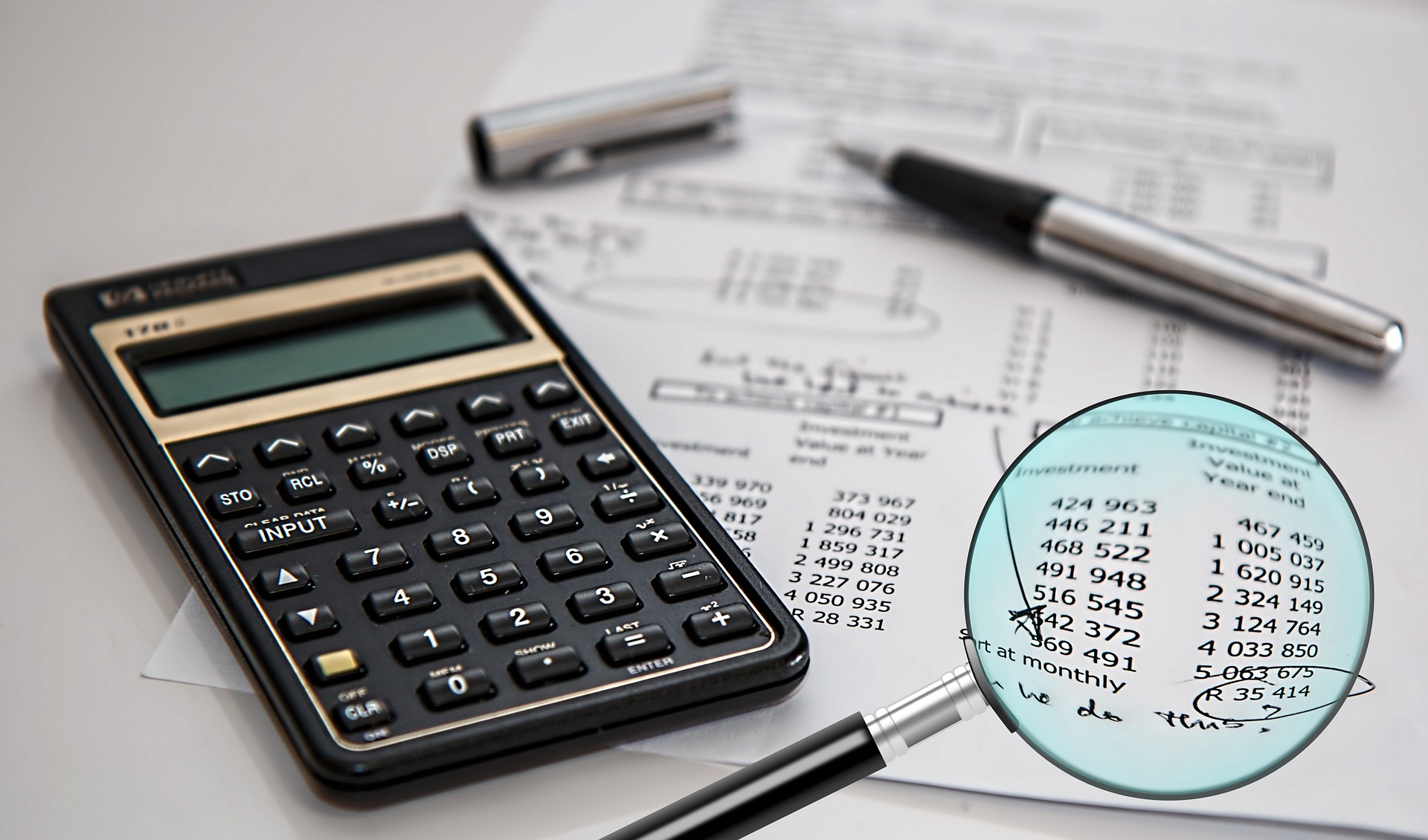 Magnifying glass held up to a piece of paper with numbers and a calculator on the side