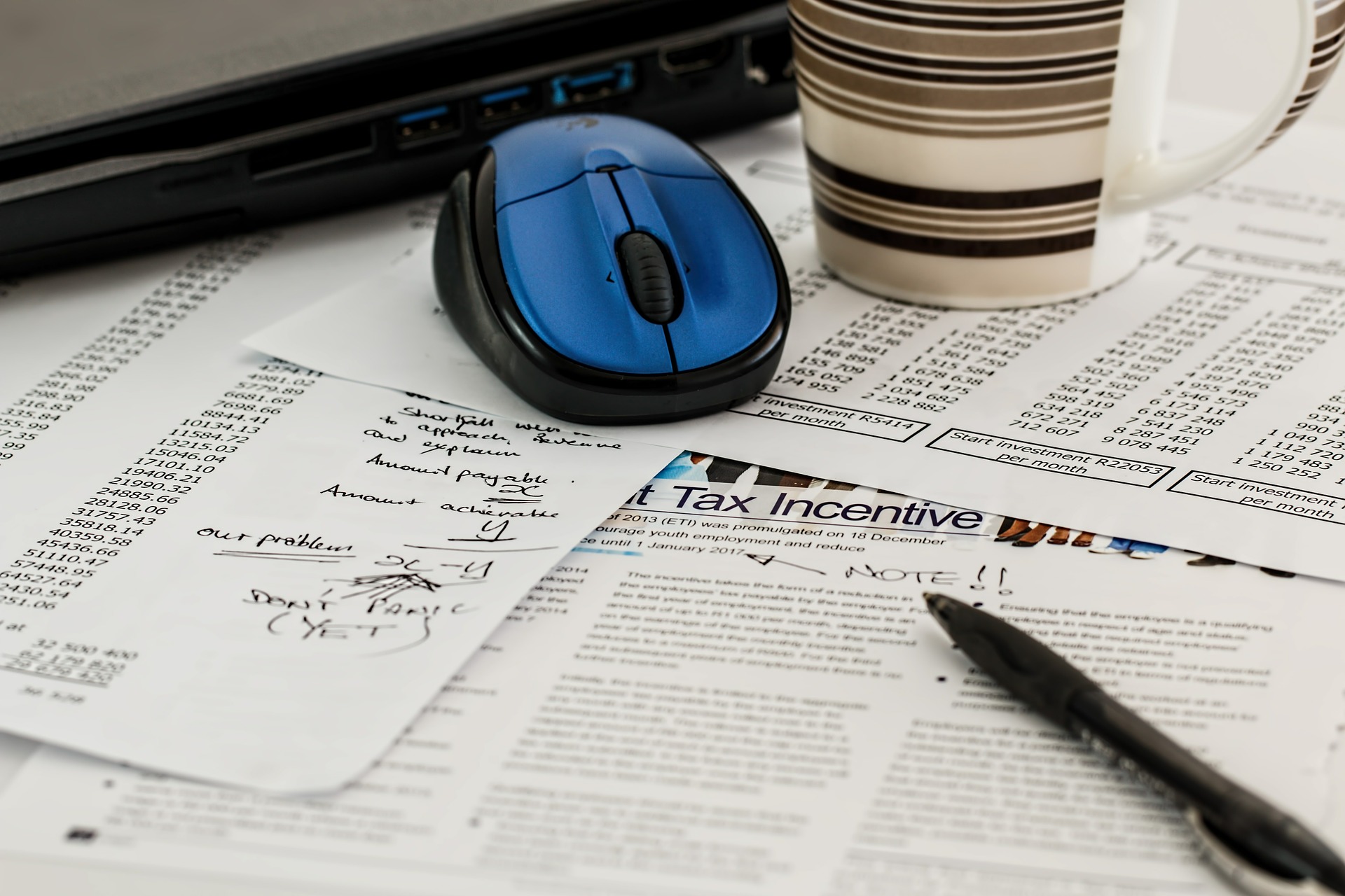 Papers spread across the table with a pen, blue mouse, and coffee cup placed on top